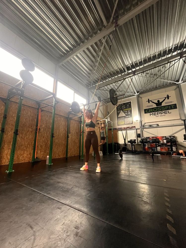 Coach Thirza tilt een halter boven haar hoofd in de zaal van CrossFit Meppel